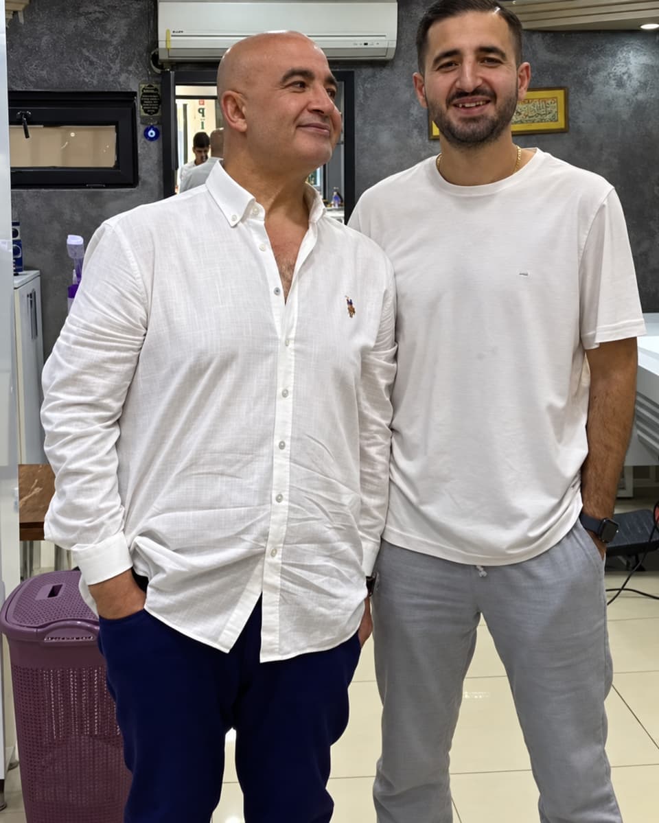 Beyaz gömlekli Ali Bey, dükkanda gülümseyen genç bir adamla yan yana duruyor